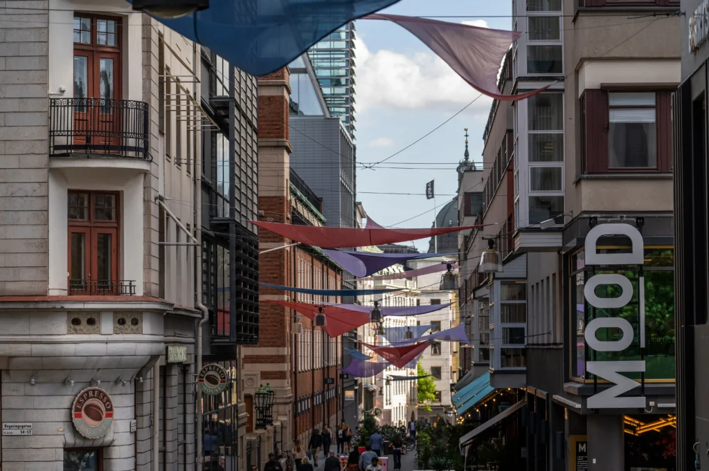 Stadsgata i Stockholm med fastigheter och butiker, färgade tyginstallationer över gatan och människor i levande innerstadsmiljö.